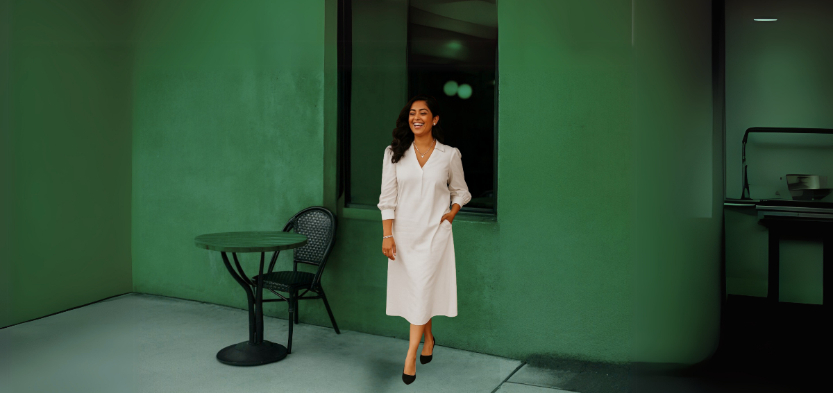 Woman in a white coat standing in a room with green walls and a table.
